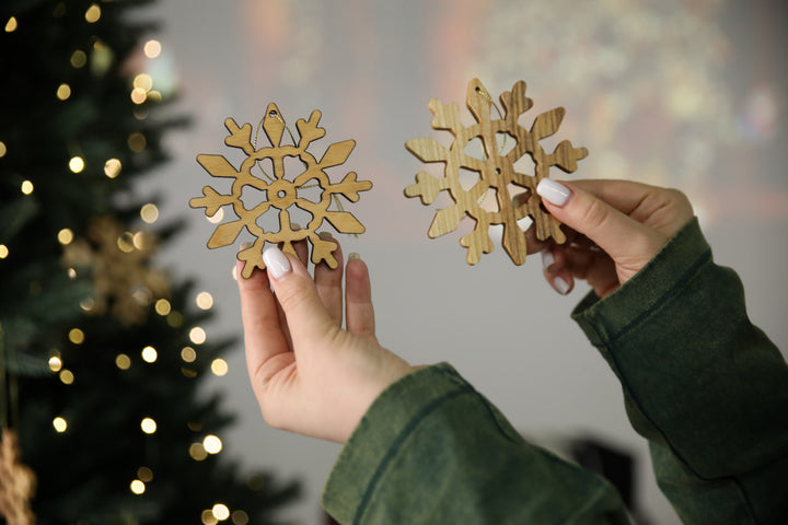 hands-holding-wooden-snowflake-ornaments-near-a-Christmas-tree-with-lights